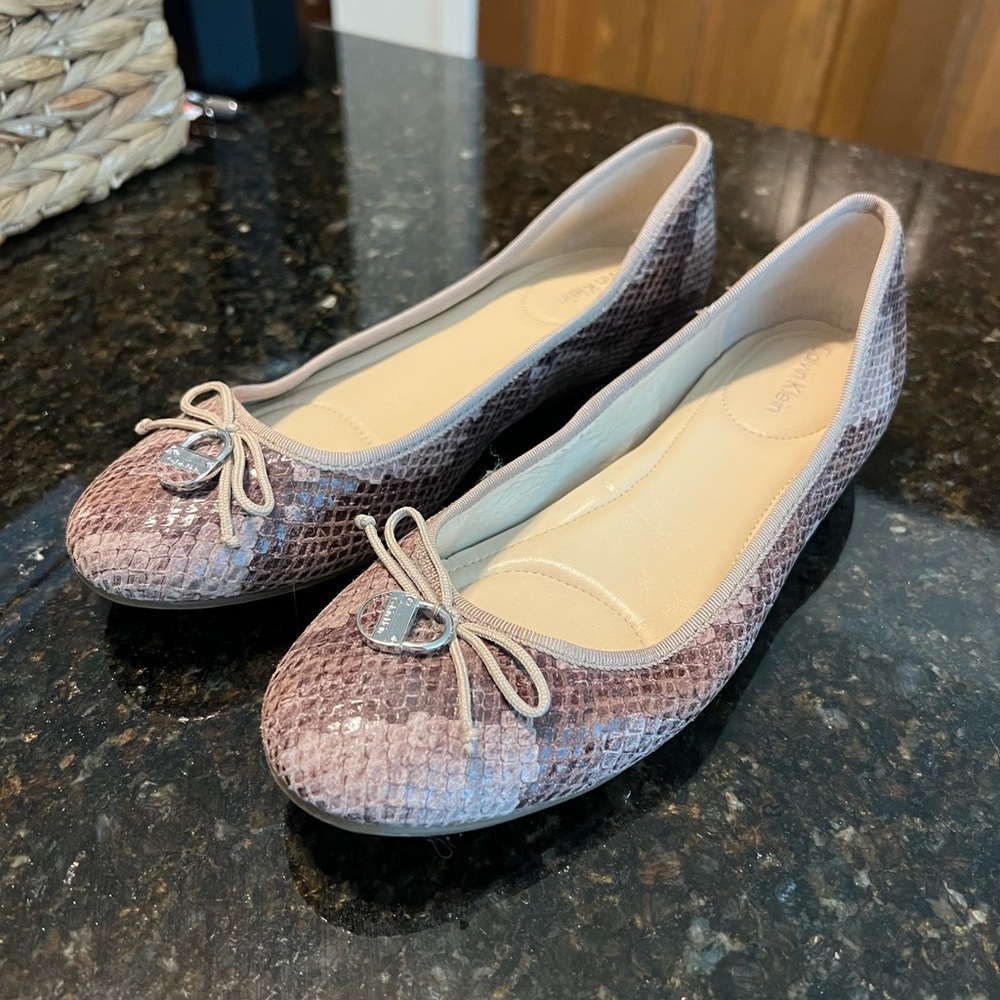 Calvin Klein snake skin flats with bow and lock motif on front.